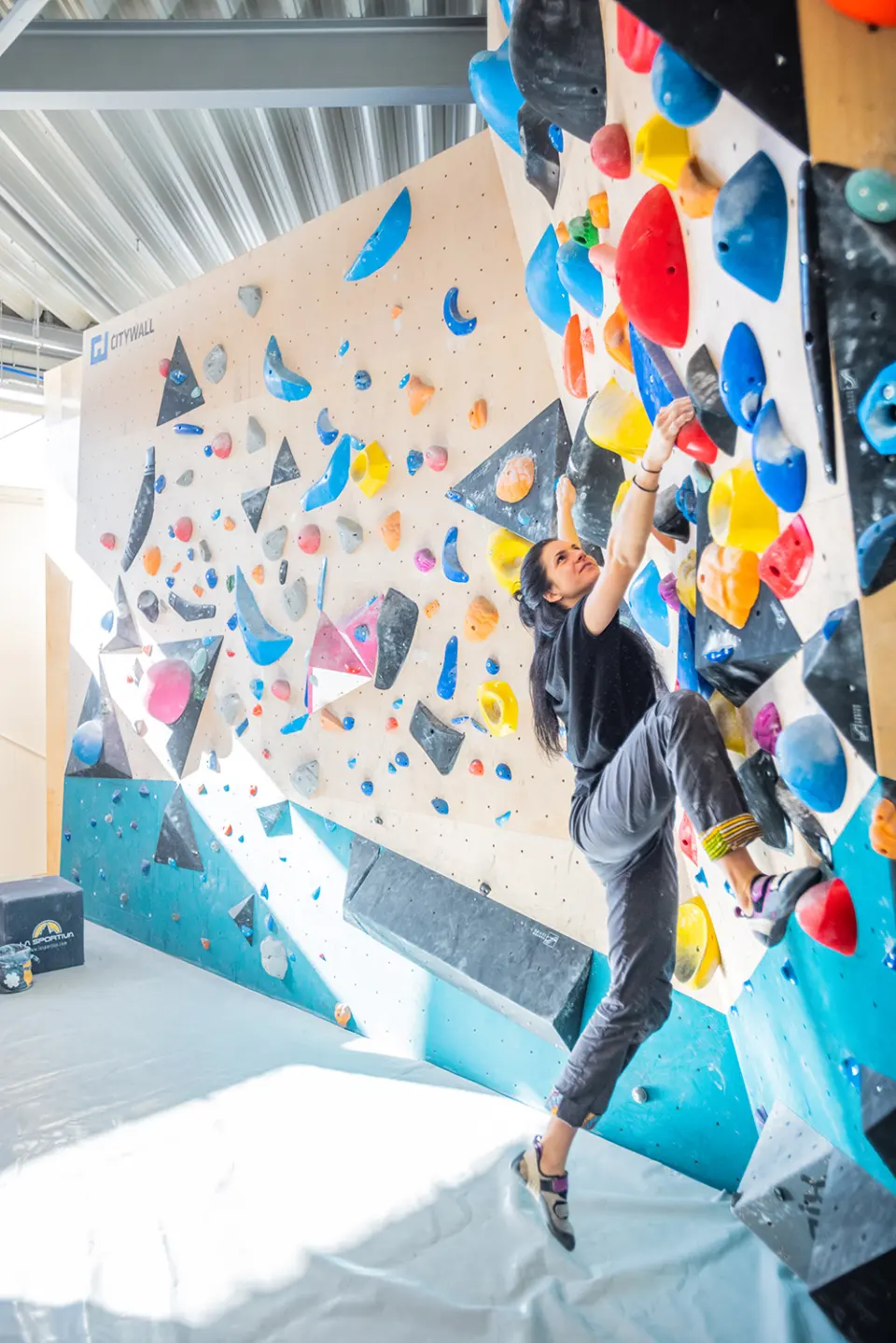 Climber reaching up an angled wall covered in colourful holds