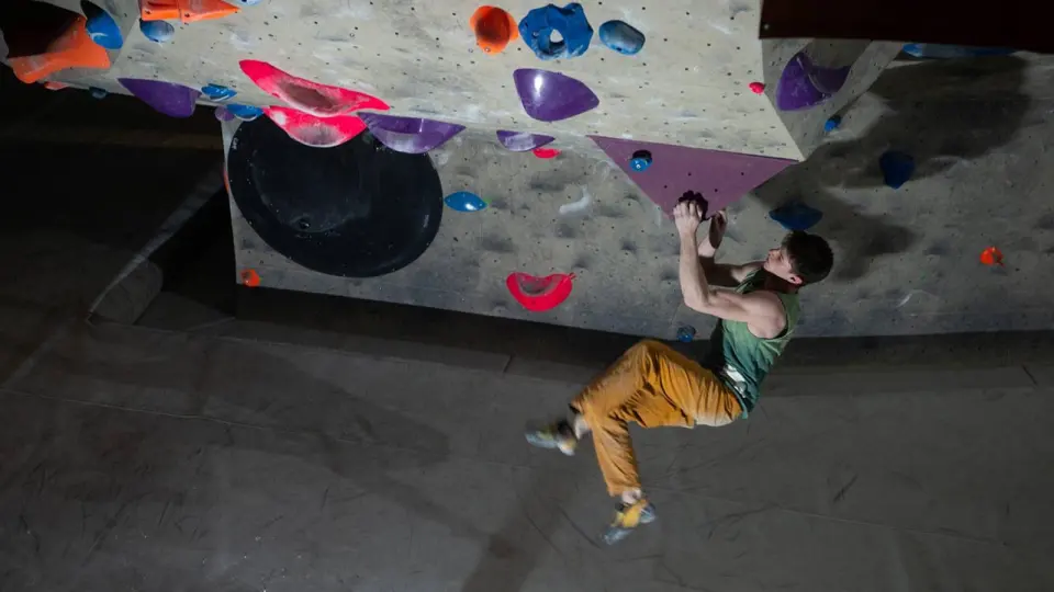Boulderer swinging from a hold under an overhang above the mats