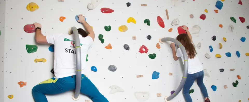 Two climbers seen from behind on a white bouldering wall with curved grey rails