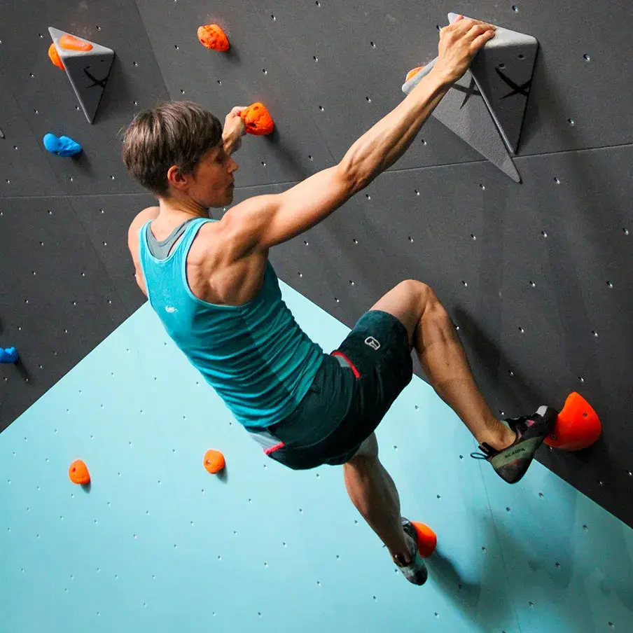 Boulderer reaching for a grey volume on a steep black and teal wall