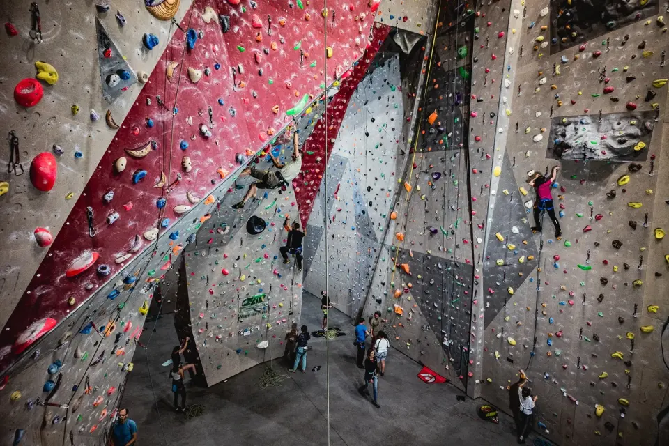 Tall roped walls with red and grey panels and several climbers on routes, seen from above