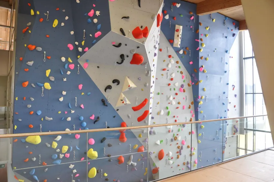Roped climbing wall with quickdraws and colourful holds behind a glass balustrade
