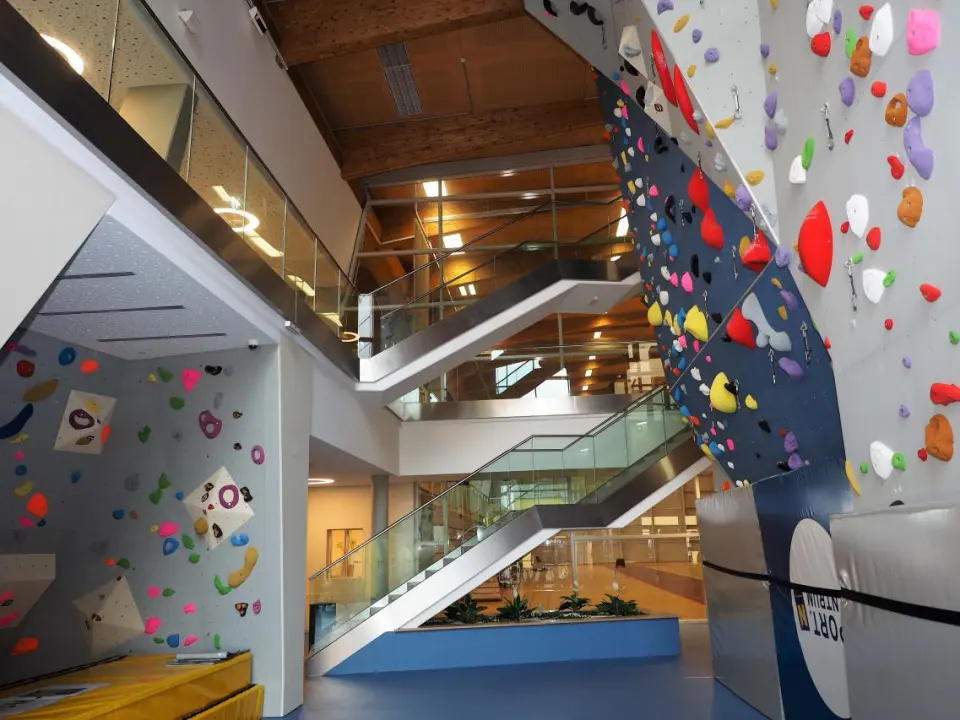 Bouldering room and roped wall in a foyer with glass staircases