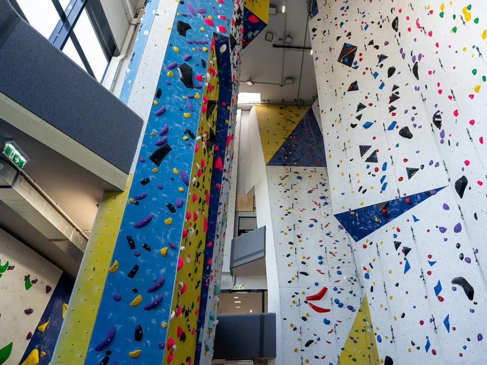 Tall roped climbing walls with colourful holds rising through the hall