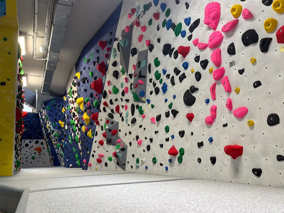 Long bouldering wall with pink, black and green holds above thick mats