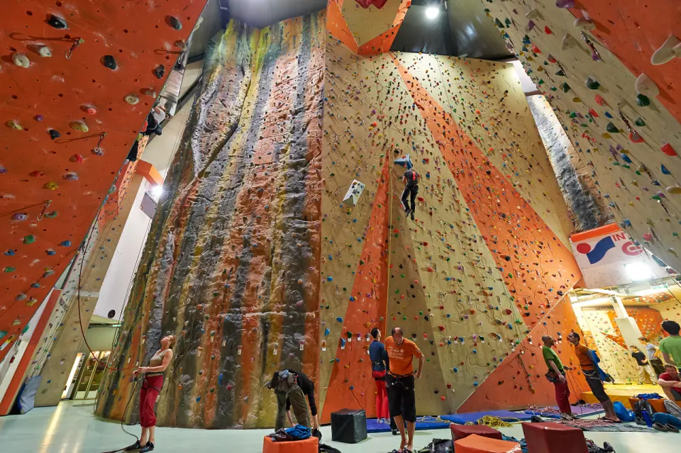 Tall orange and grey lead walls with a climber high up and belayers below