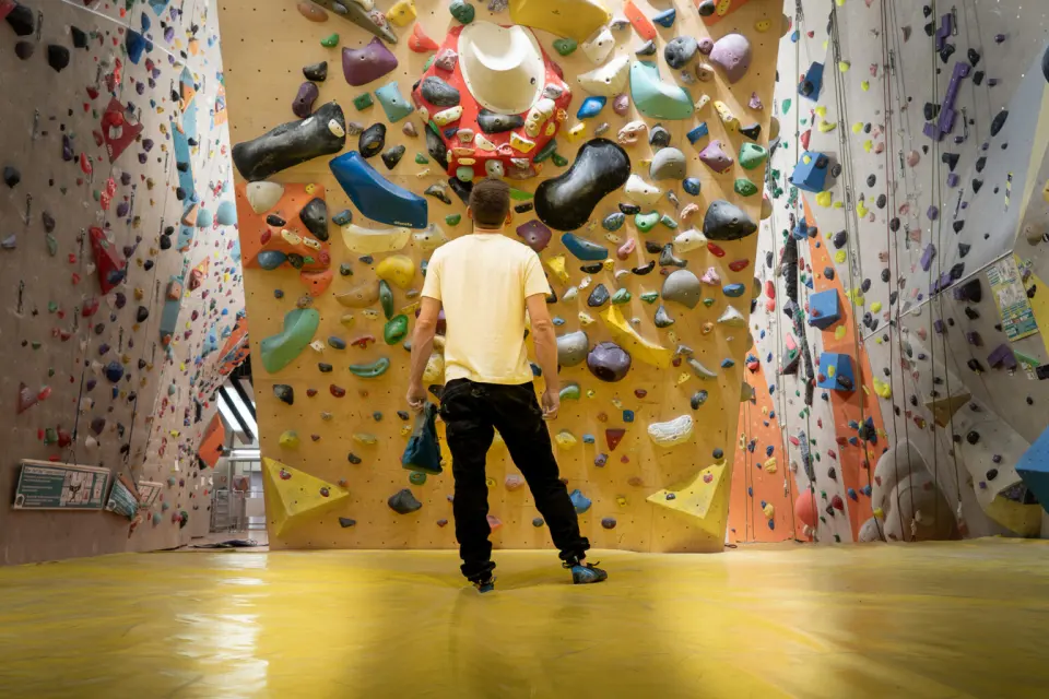 Climber facing a bouldering wall of big holds between tall roped walls