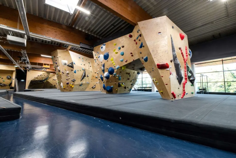 Angular wooden bouldering blocks above thick grey mats under a timber roof
