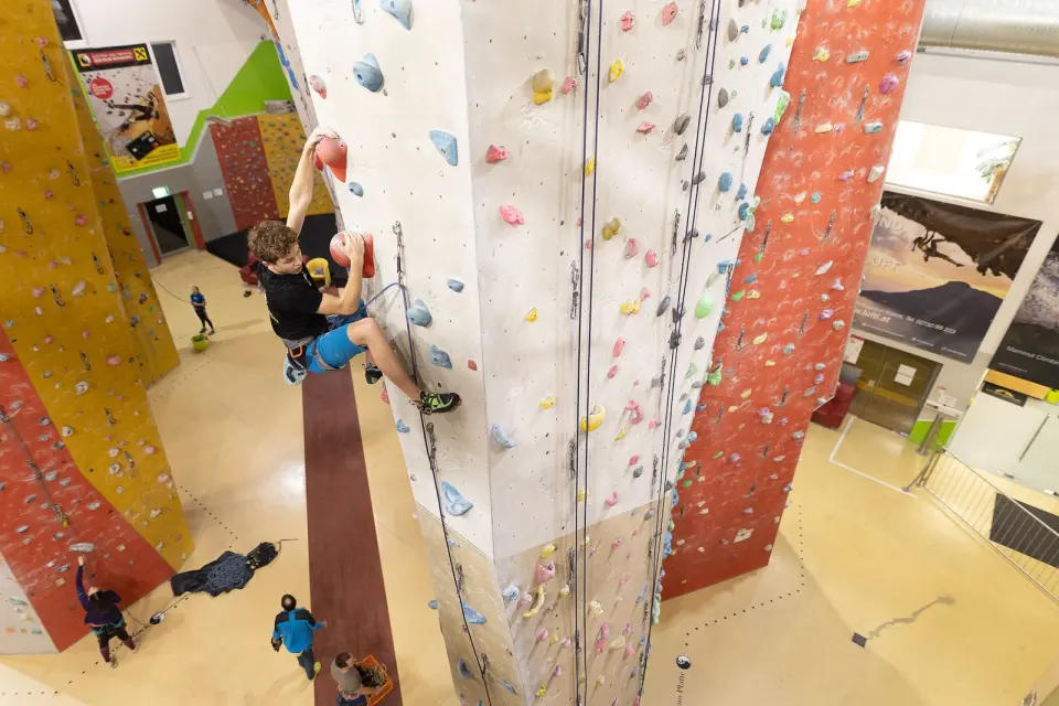 Climber on a tall pillar of lead routes high above the hall floor