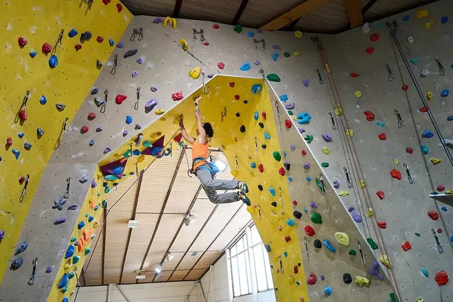 Climber on a roped route under a yellow roof between tall grey walls