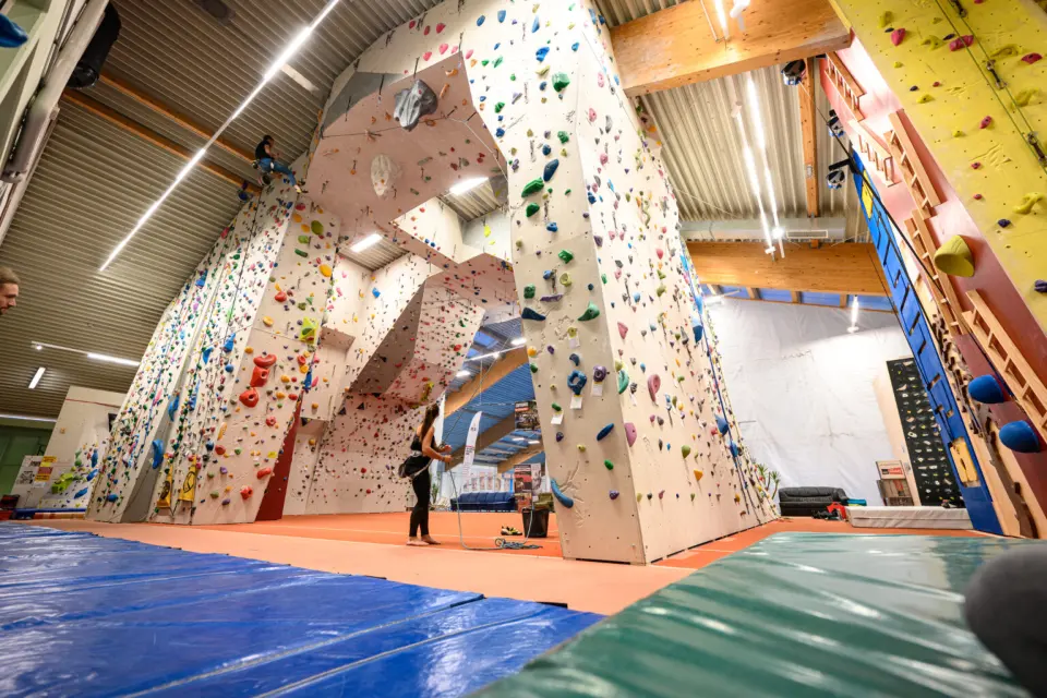 Tall lead walls with a climber high on a route and a belayer below
