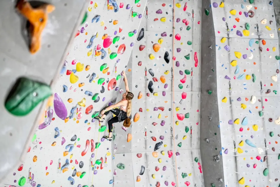 Climber high on a tall lead wall covered in colourful holds