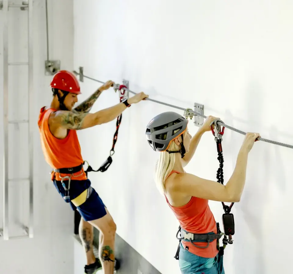 Two climbers in helmets clipped to the cable of the indoor via ferrata