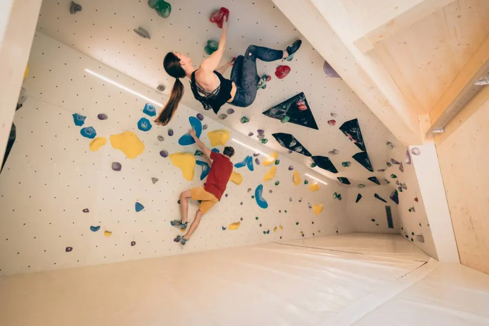 Two climbers on a bouldering wall with colourful holds under a timber ceiling