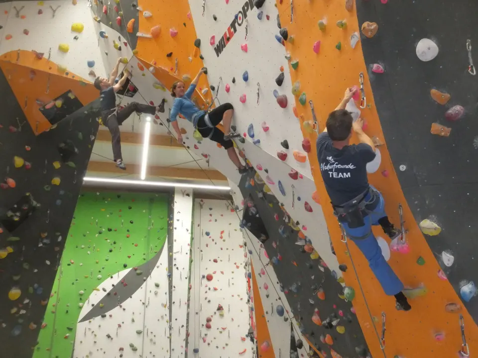 Three climbers leading on orange, grey and white walls, with a green wall behind