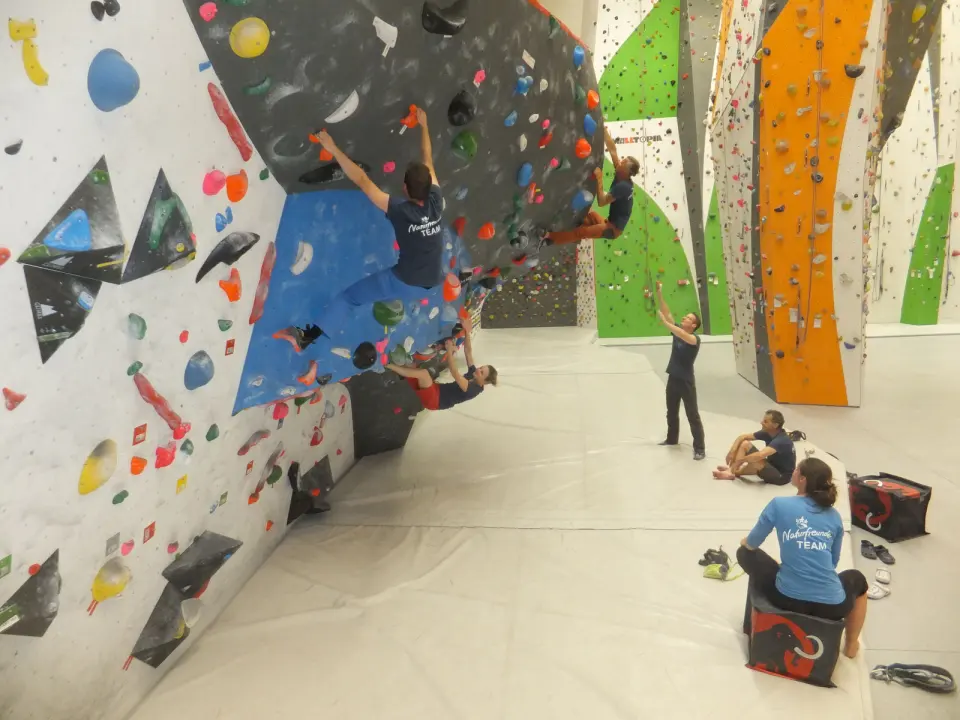 Climbers on an overhanging boulder wall, with lead walls in the background