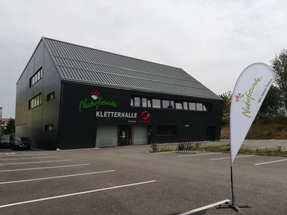 Dark grey climbing hall building with its car park