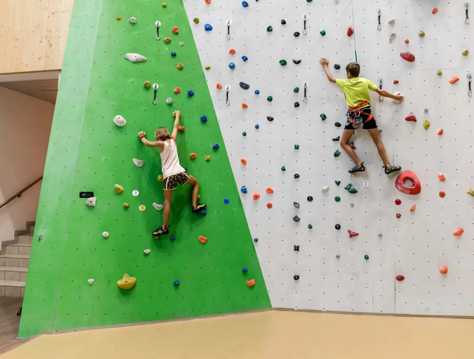 Two young climbers on roped routes on a green and grey climbing wall