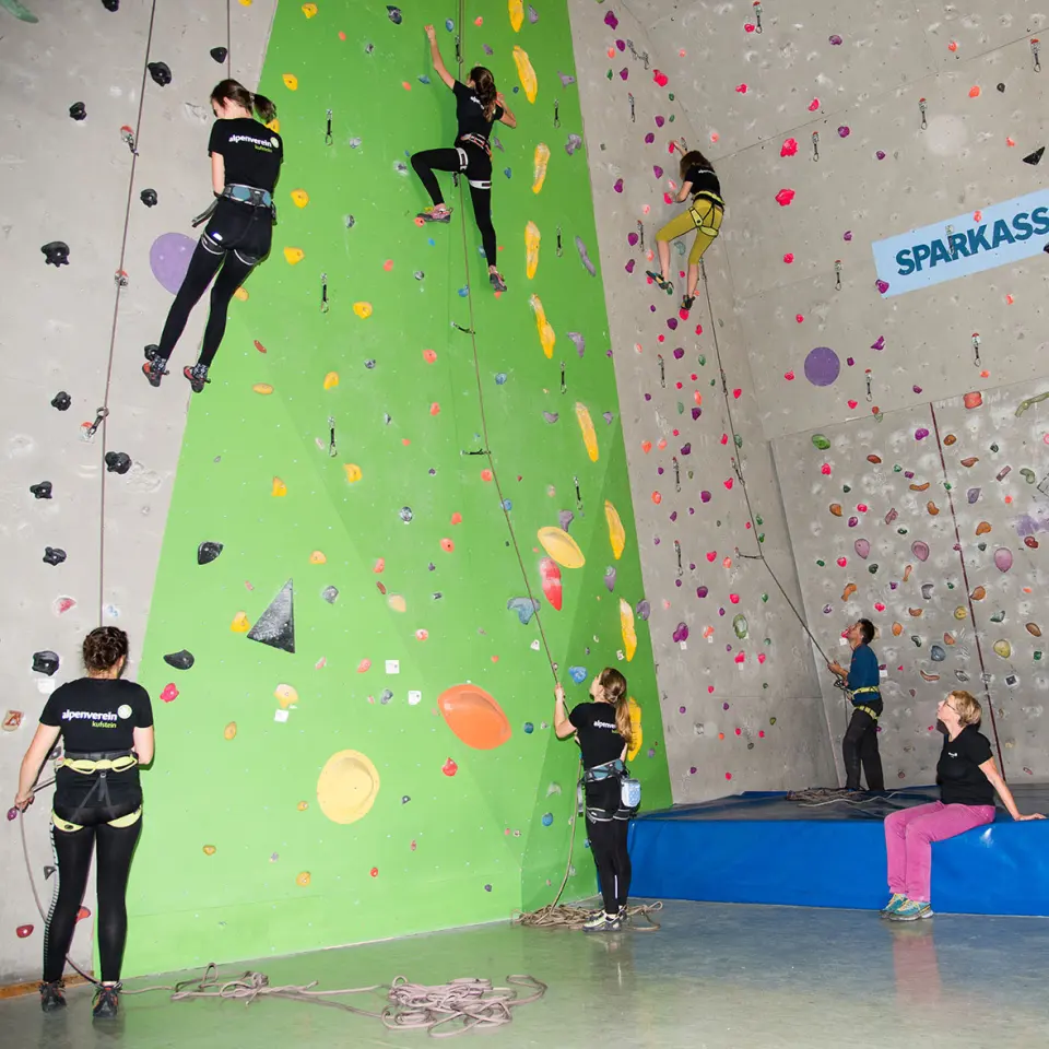 Climbers on roped routes on green and grey walls, with belayers below