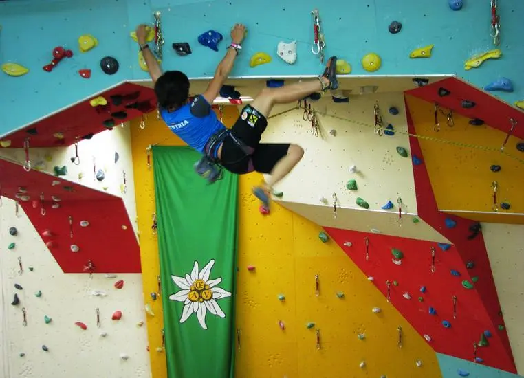 Climber pulling over a roof on a yellow, red and blue lead wall with an Alpenverein banner