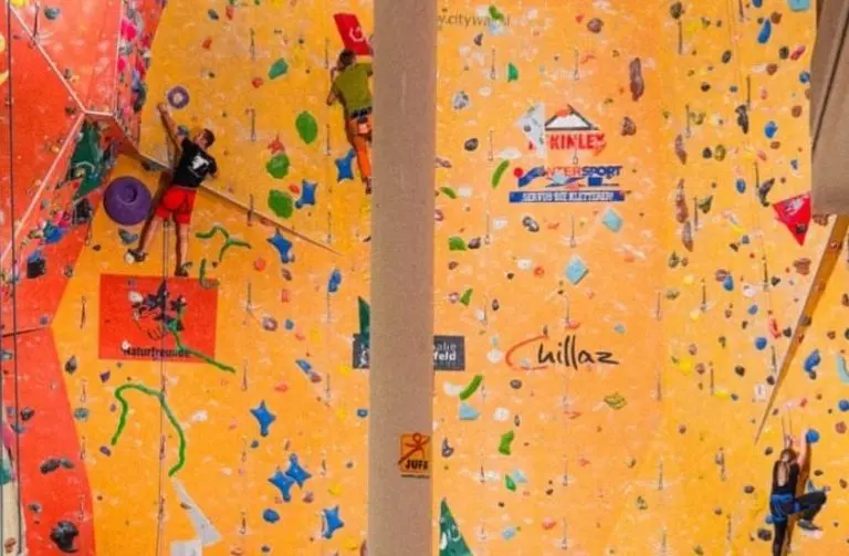Climbers on roped routes up the orange and red lead walls