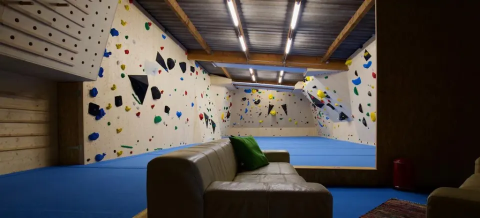 Bouldering hall with wooden walls, blue matting and a leather sofa in the foreground