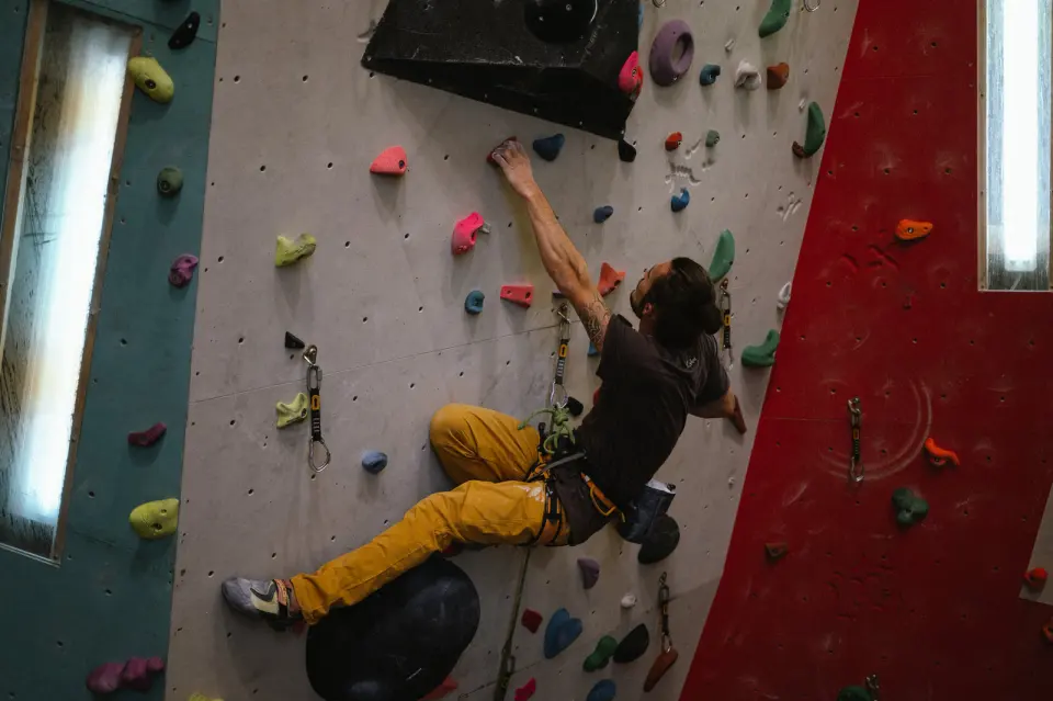 Climber clipping a quickdraw on a grey lead wall between red and teal panels