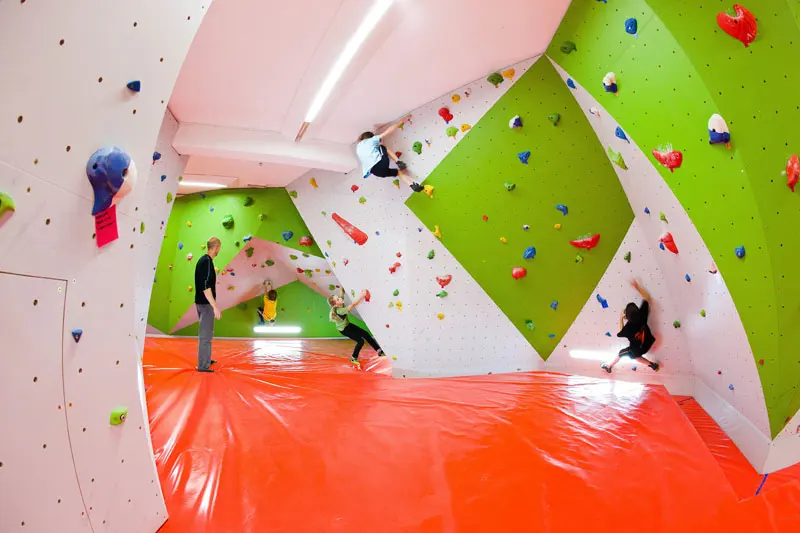 Bouldering room with angled green and white walls above orange mats
