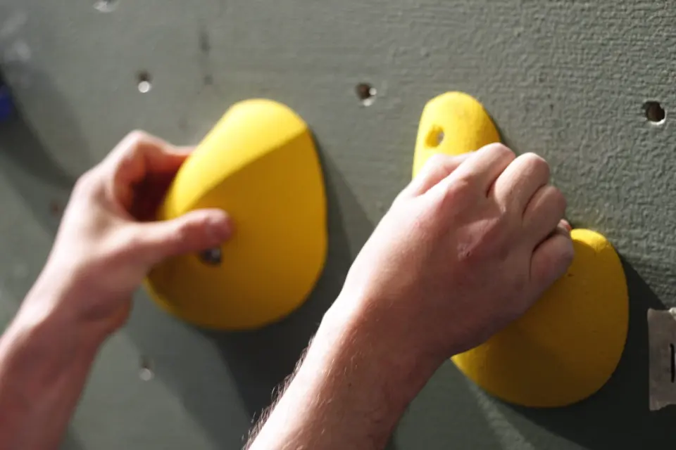 Hands gripping two yellow holds on a grey-green wall