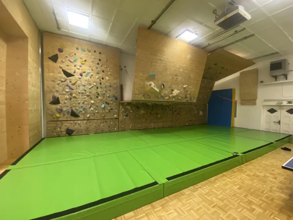 Bouldering wall with its adjustable panels set at a gentler angle, seen across the green mats