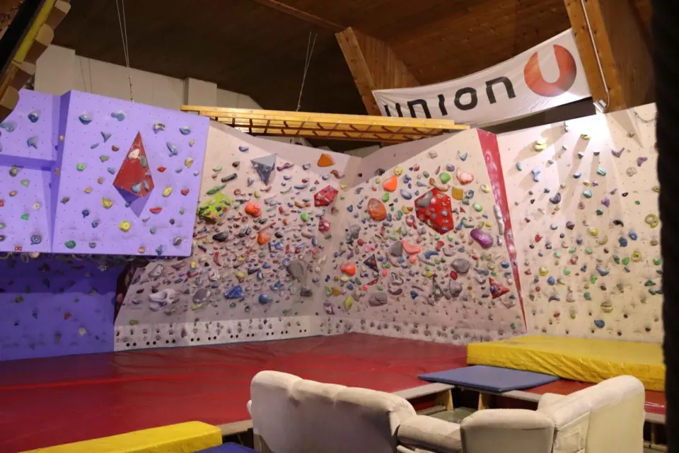 Purple and white bouldering walls above red mats, with wooden rungs under the roof