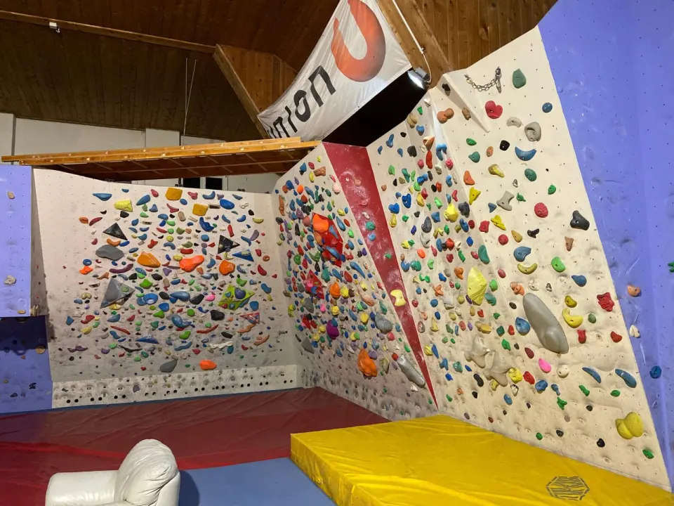 Angled white bouldering walls with a red arete and a yellow crash mat
