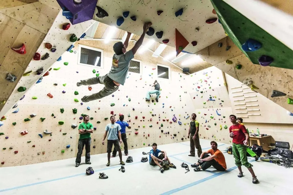 Climber swinging from a steep wooden overhang as others watch in the barn bouldering hall