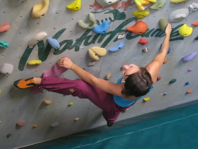 Climber reaching across a grey bouldering wall covered in coloured holds