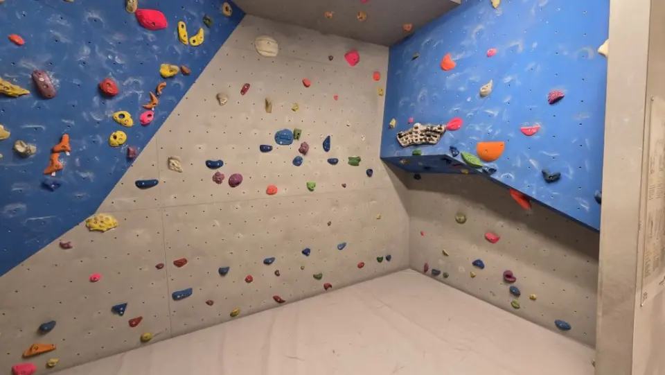 Bouldering room with an overhanging blue wall above padded matting