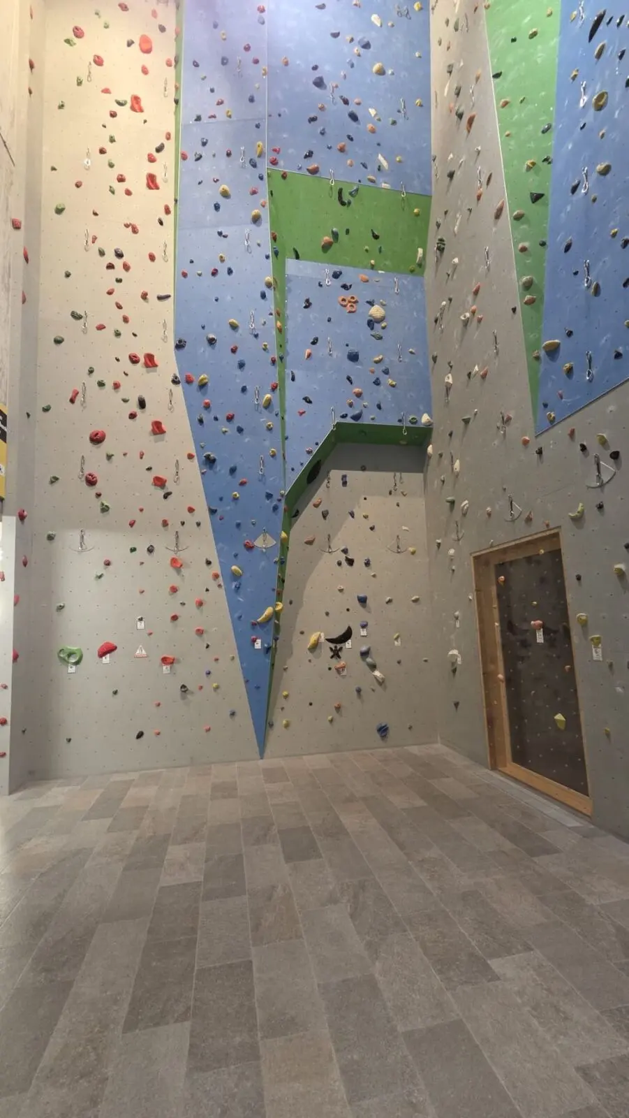 Tall climbing walls with quickdraws above a tiled floor