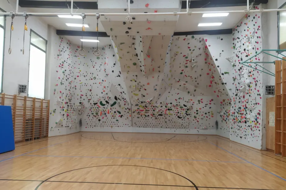 White climbing wall with a steep central overhang filling one end of a sports hall