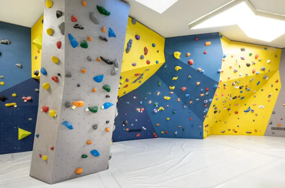 Blue, yellow and grey bouldering walls around a free-standing pillar above white mats