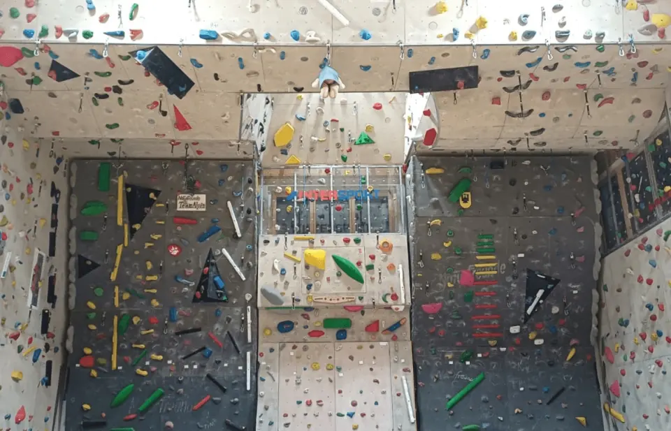 Roped climbing walls with an overhanging roof section and coloured holds in a school gym
