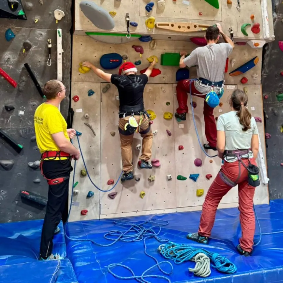 Two climbers on top rope above blue mats, with their belayers below