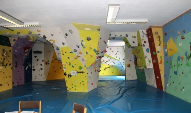 Bouldering room with angled yellow, white and green walls and blue mats