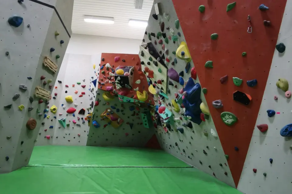 Angled bouldering walls in grey and red with green mats and an overhang at the back
