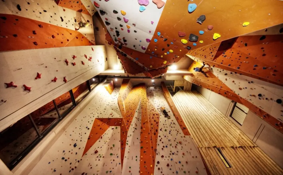 Looking up at tall orange and white lead walls and a steep overhang, with climbers high on the routes