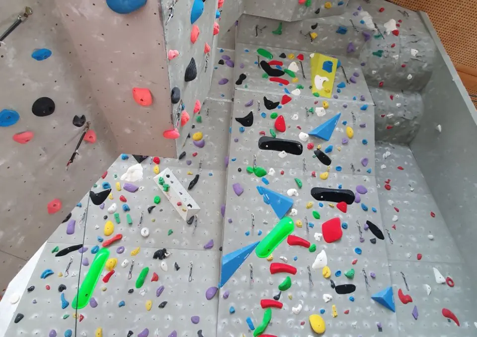 Grey climbing walls with colourful holds, volumes and quickdraws below a steep roof