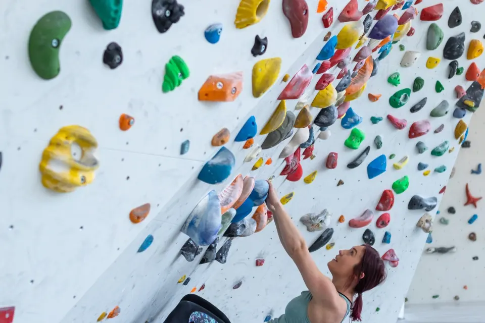 Climber reaching up an overhanging white bouldering wall densely set with colourful holds