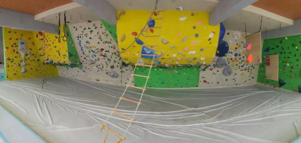 Bouldering walls around the matted floor of a former swimming pool, with a rope ladder