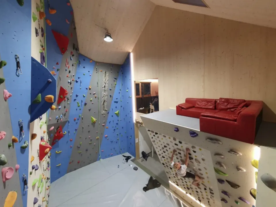 Blue and grey lead walls with a crack, and a lit MoonBoard below a lounge gallery with a red sofa
