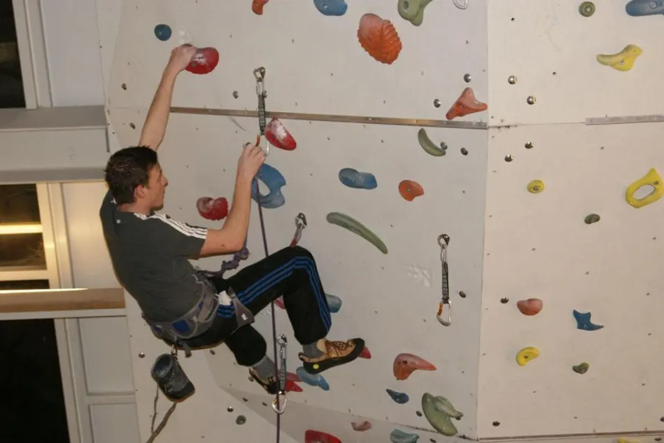 Lead climber clipping a quickdraw on a white wall with coloured holds