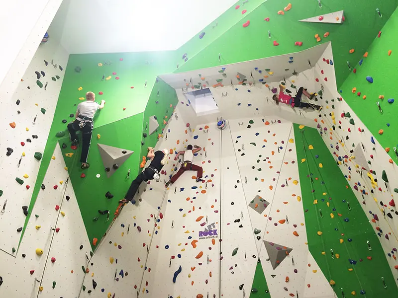 Climbers on roped routes up green and white walls with an overhang