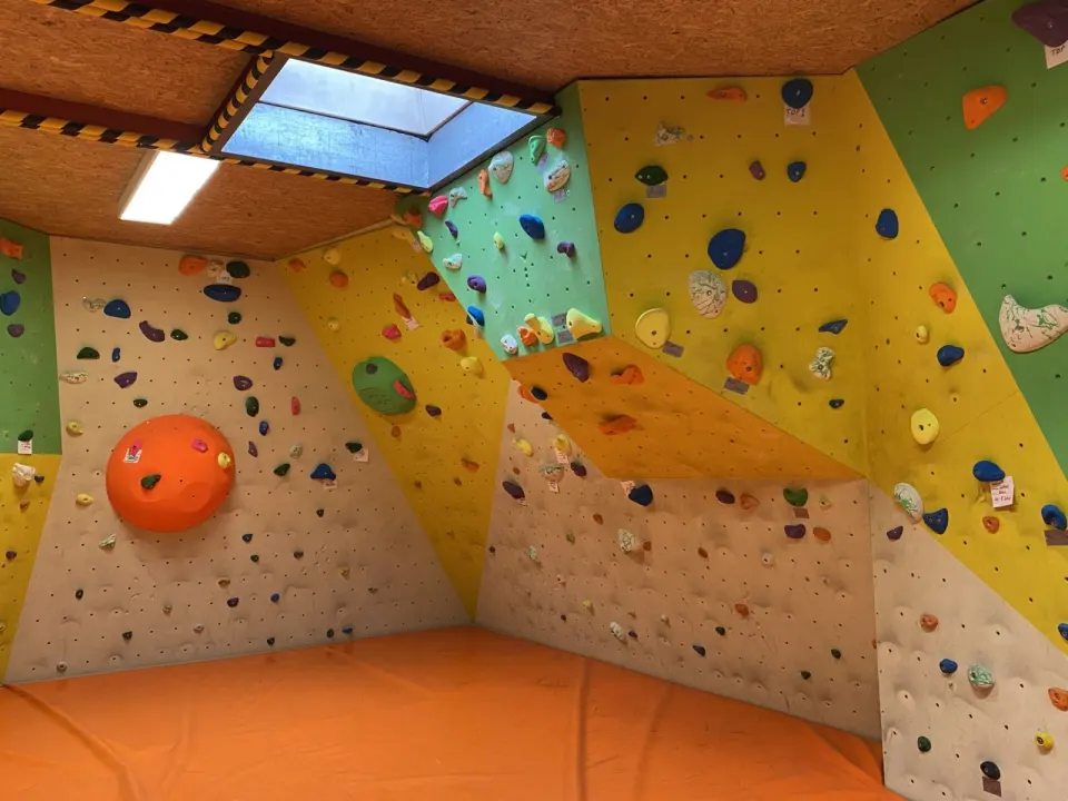 Small bouldering room with yellow, green and white walls, an orange volume, a skylight and orange mats